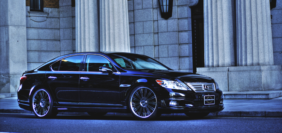 Black WALD Executive Line Lexus LS460L side profile beside classical stone columns