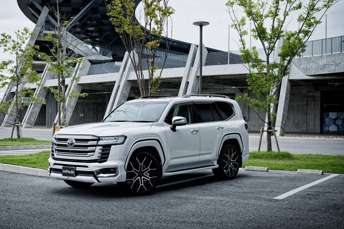 White Toyota Land Cruiser LC300 with WALD ELDORANTE E11C 24-inch wheels — front three-quarter view in an urban setting