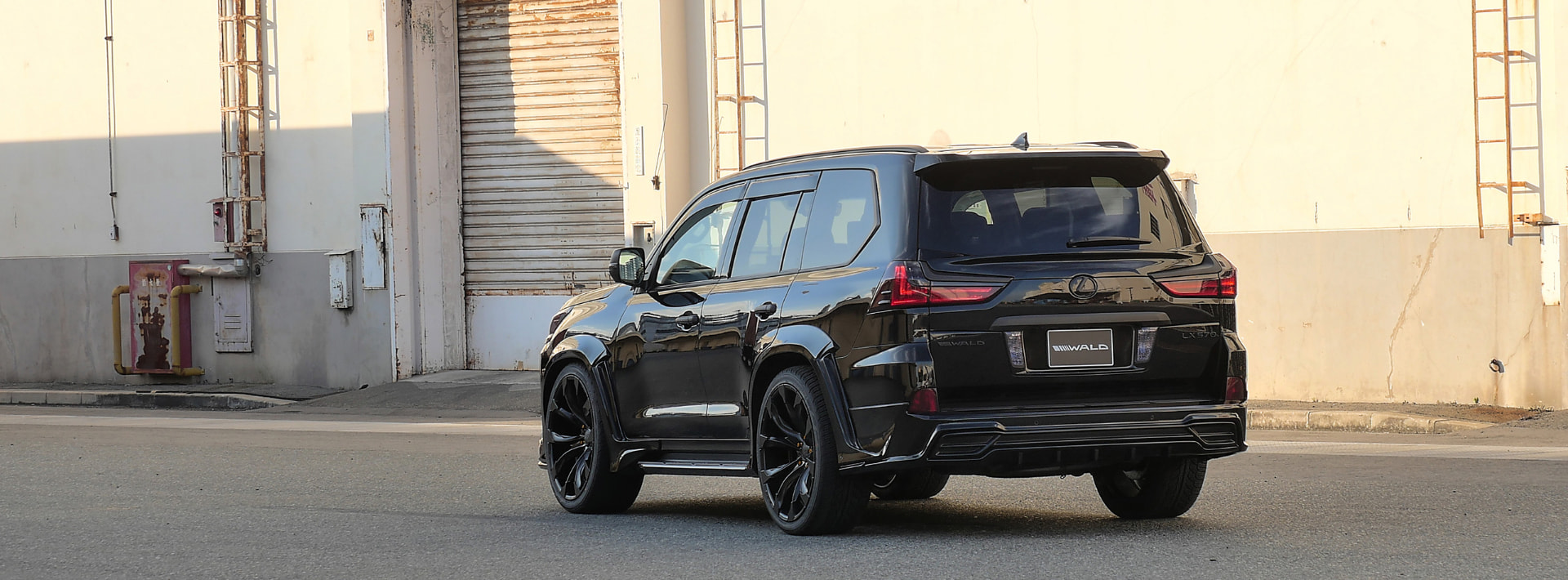 Black WALD Lexus LX570 rear three-quarter view showing tailgate spoiler, rear skirt and wide over fenders
