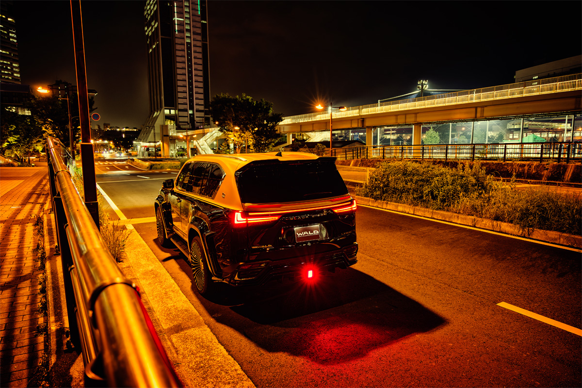 WALD Lexus LX600 Black Bison rear night view — WALD rear skirt LED lamp and side exit exhaust glowing under street lighting