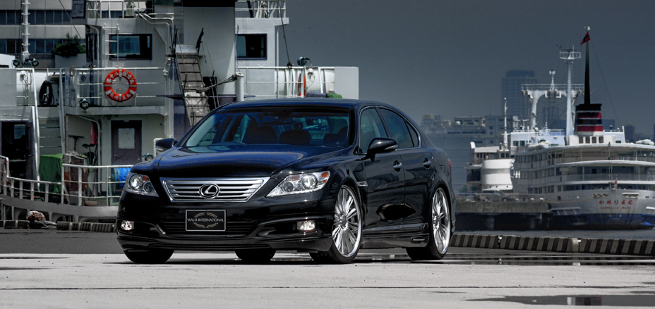 Black WALD Executive Line Lexus LS460L front three-quarter view at a harbour quayside