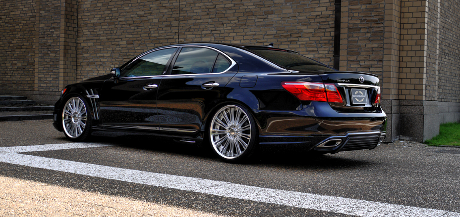 WALD Executive Line Lexus LS600h rear three-quarter view beside a brick wall on chrome WALD wheels