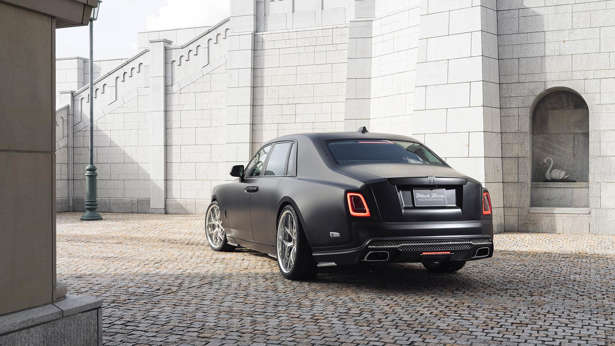 Rear three-quarter view of a matte black Rolls-Royce Phantom Black Bison fitted with WALD ILLIMA I13F forged wheels