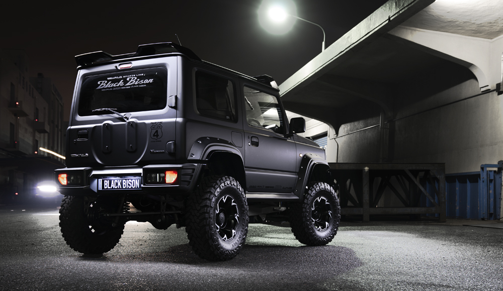 WALD Black Bison Edition Suzuki Jimny JB74W — rear three-quarter night view with spare tyre cover, rear bumper spoiler and Black Bison graphics