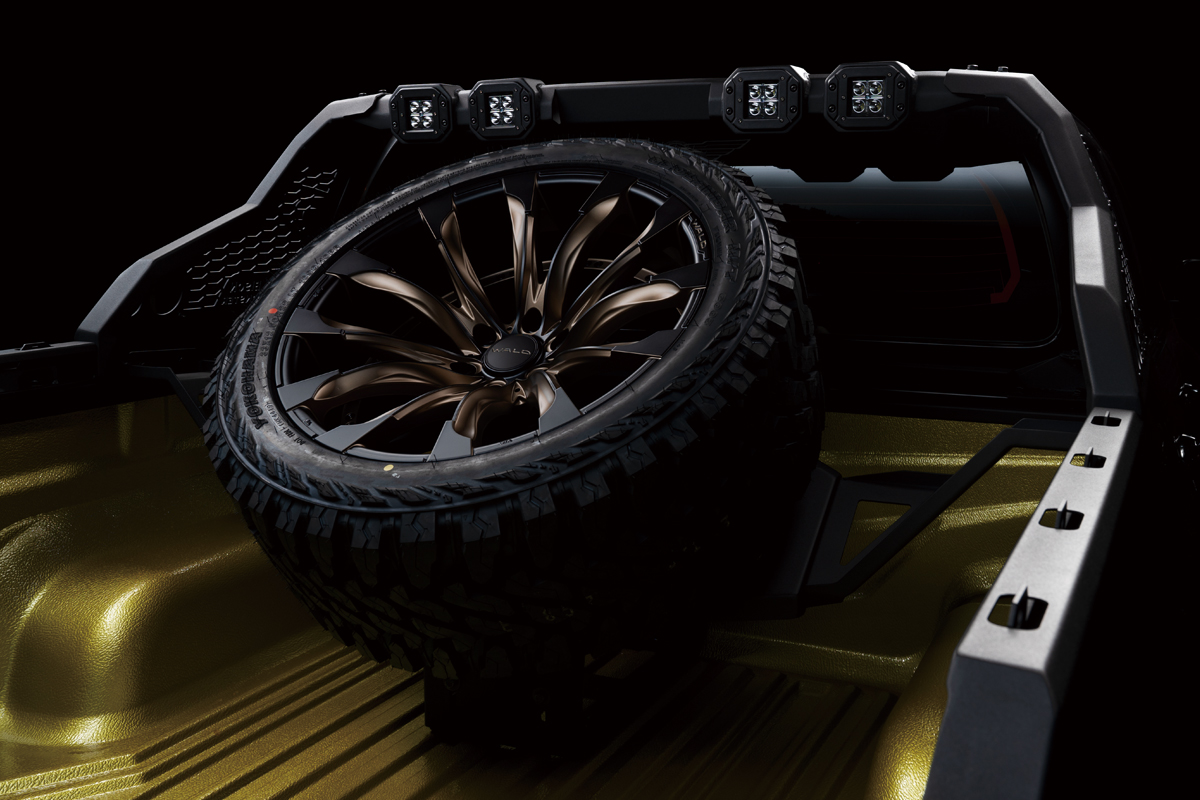 Bronze WALD wheel and off-road tyre mounted on the Black Bison spare tyre hanger in the Hilux bed