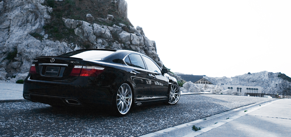 Black WALD Executive Line V1 Lexus LS460L rear three-quarter view on a coastal quarry road