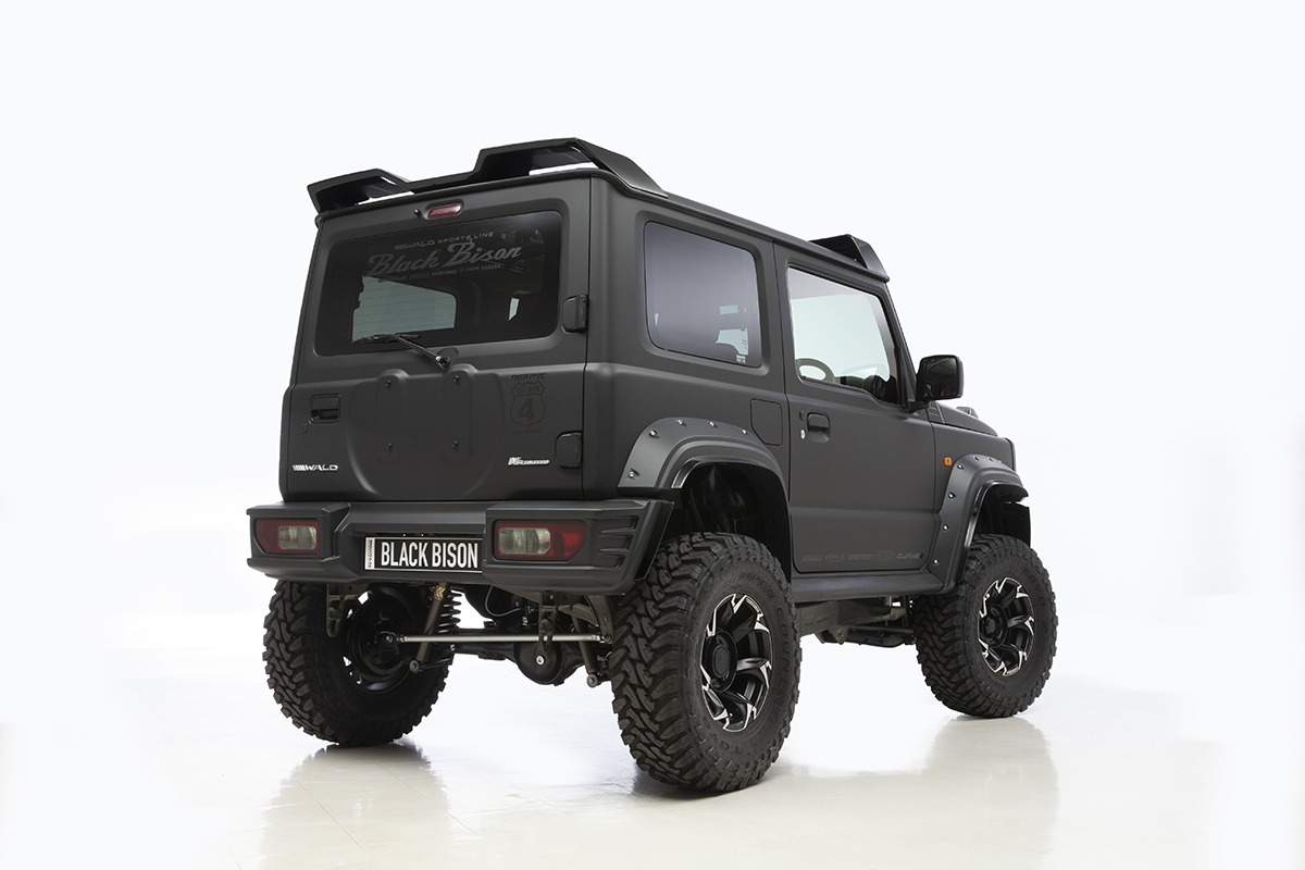 WALD Black Bison Edition Suzuki Jimny Sierra JB74W — matte black wide body Jimny rear three-quarter studio view with rear wing, spare tyre cover and rear bumper spoiler