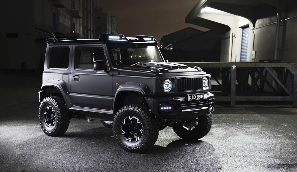 WALD Black Bison Edition Suzuki Jimny Sierra JB74W — front three-quarter night view with Japamericana grill, aero bonnet and roof LED light bars