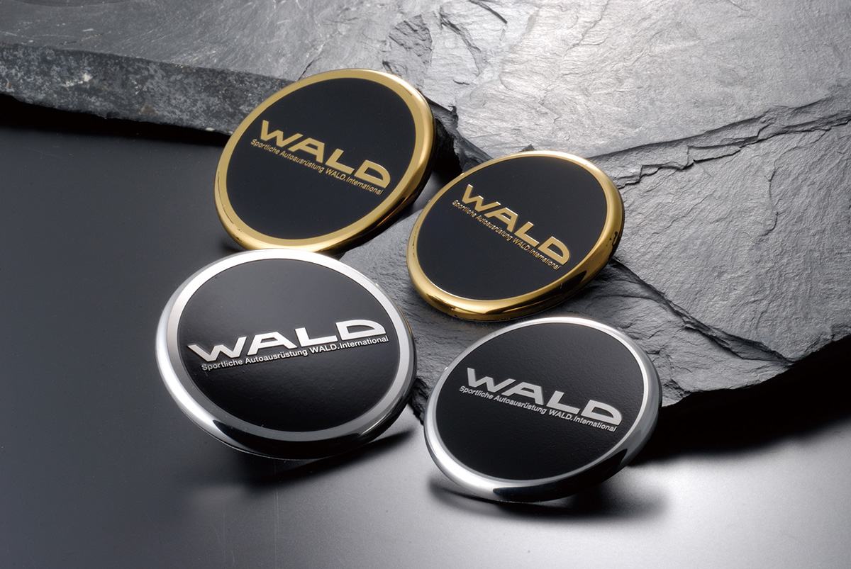 WALD Metal Hood Badges in chrome and gold finishes with black centres, arranged on dark slate