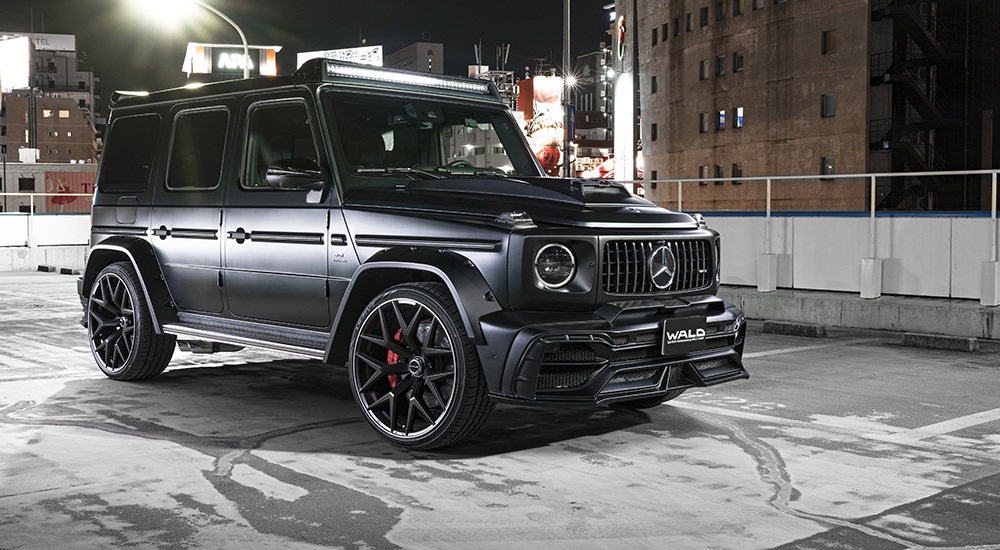 WALD Black Bison Mercedes-AMG G63 W463A night city front three-quarter — black G63 with wide arches, bonnet scoop and illuminated roof LED bar