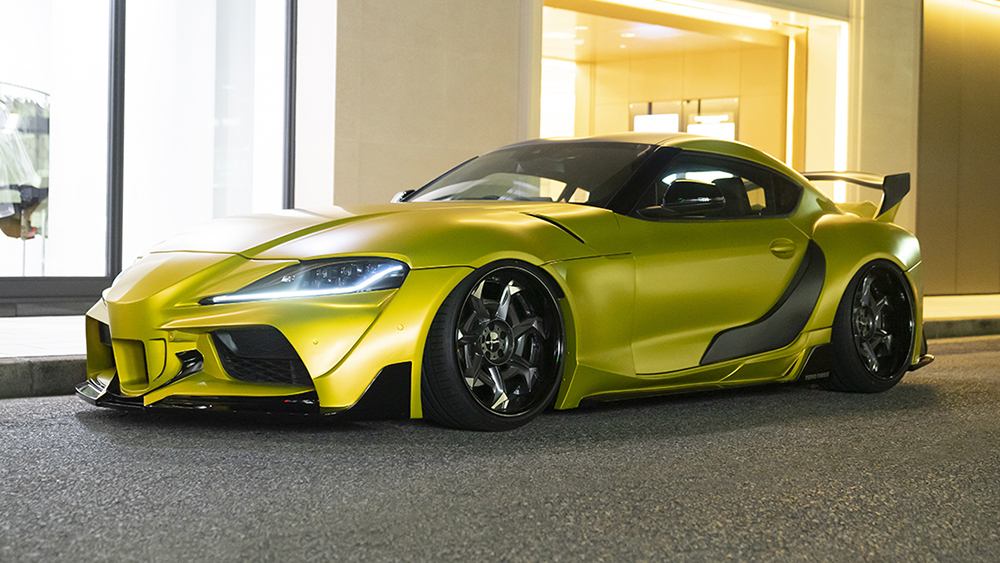 WALD Sports Line Wide Body Toyota Supra DB## in matte yellow, front three-quarter view at night with wide front fenders and side skirts