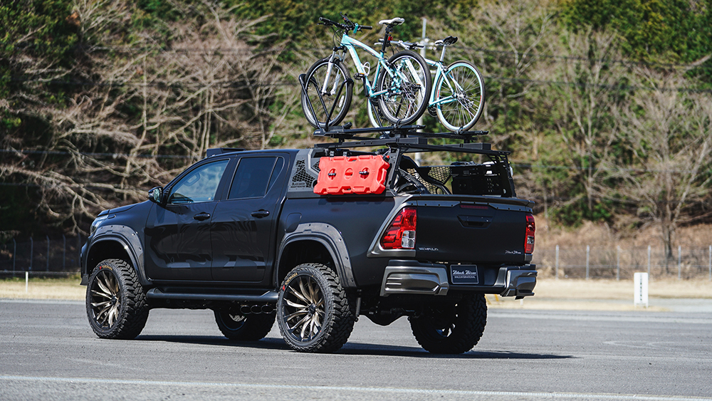 Rear three-quarter view of the WALD Black Bison Toyota Hilux GUN125 with bed rack and bicycles