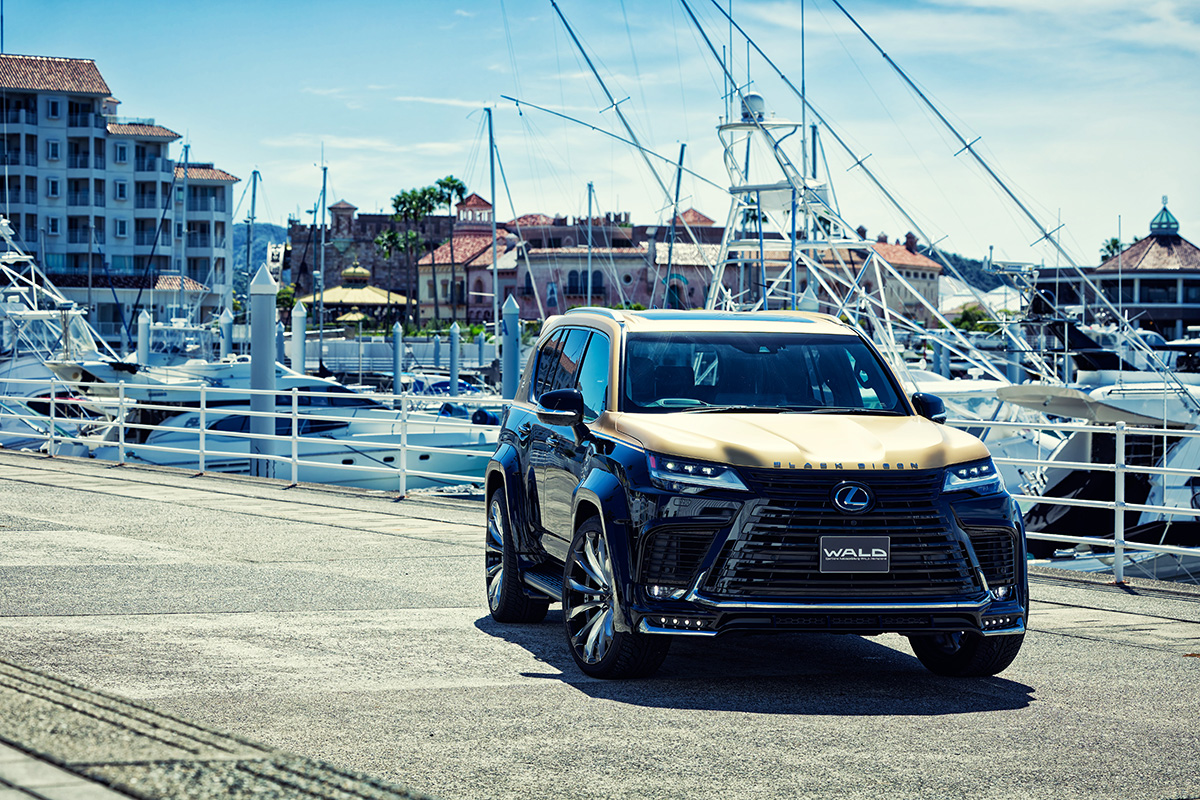 WALD Black Bison Lexus LX600 front three-quarter view at a marina — black and gold two-tone with WALD grille garnish