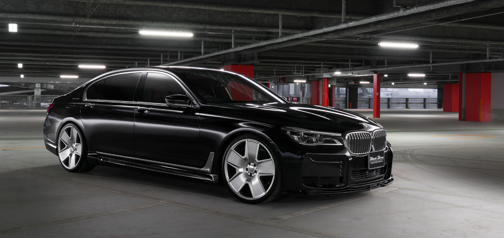 WALD BMW 7 Series G12 Black Bison body kit on a black 7 Series, front three-quarter view in a parking structure