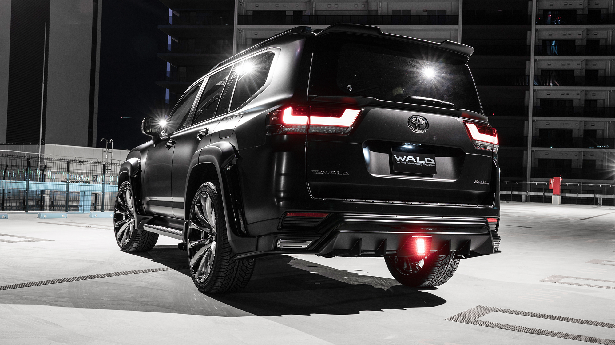 WALD Black Bison Land Cruiser 300 ZX rear three-quarter night view with tailgate spoiler and rear skirt diffuser