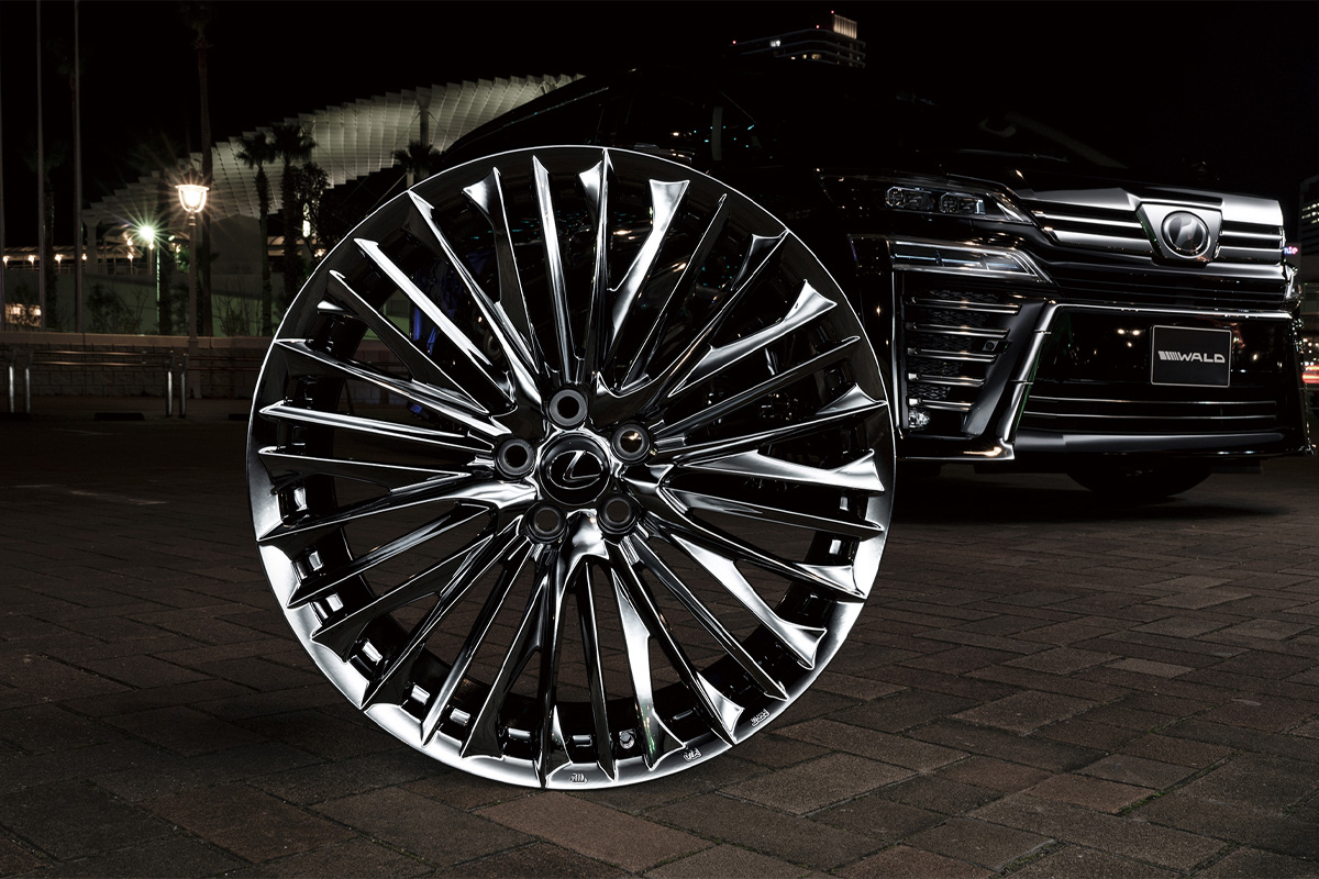 WALD Genuine Line F-001 wheel in SBC Super Black Coat displayed at night beside a black Lexus with WALD front bumper