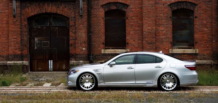 WALD Executive Line V2 Lexus LS600h side profile in silver beside a red brick warehouse on polished WALD wheels