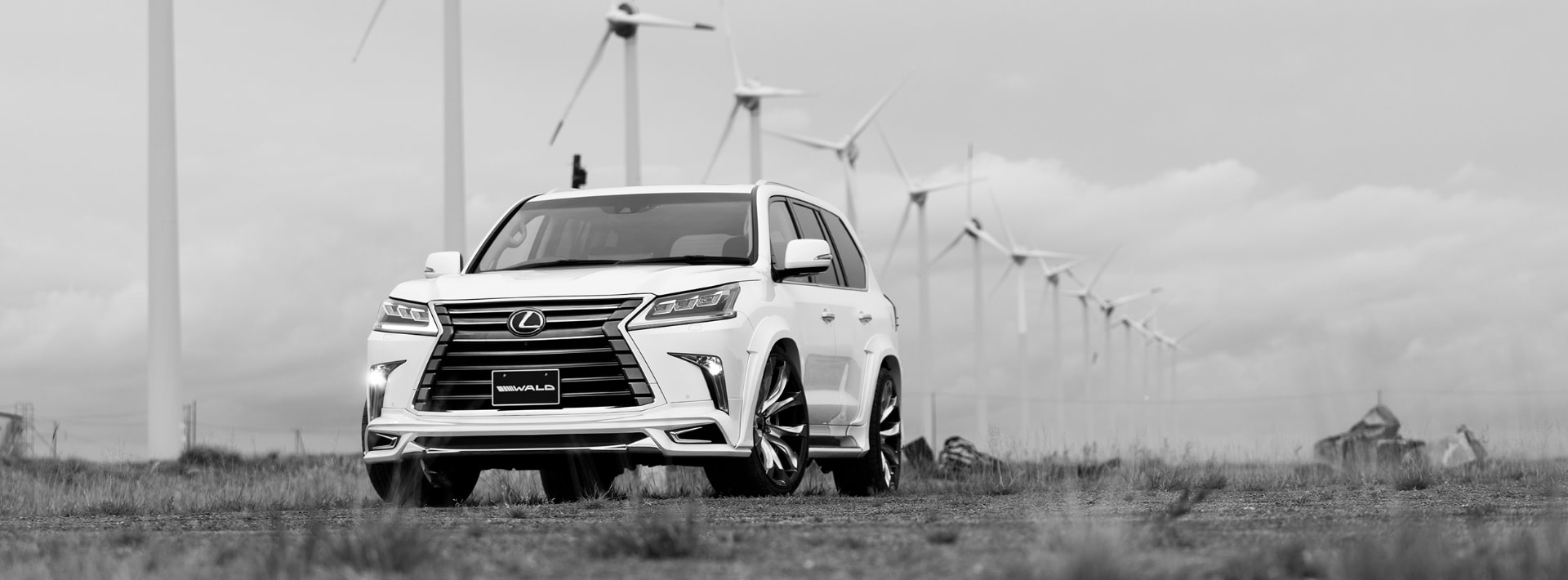 White WALD Lexus LX570 Sports Line front three-quarter view photographed at a wind farm