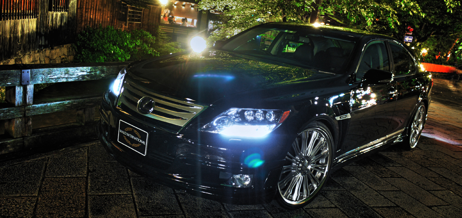 WALD Executive Line Lexus LS600h front three-quarter night view on a cobbled street with headlights lit