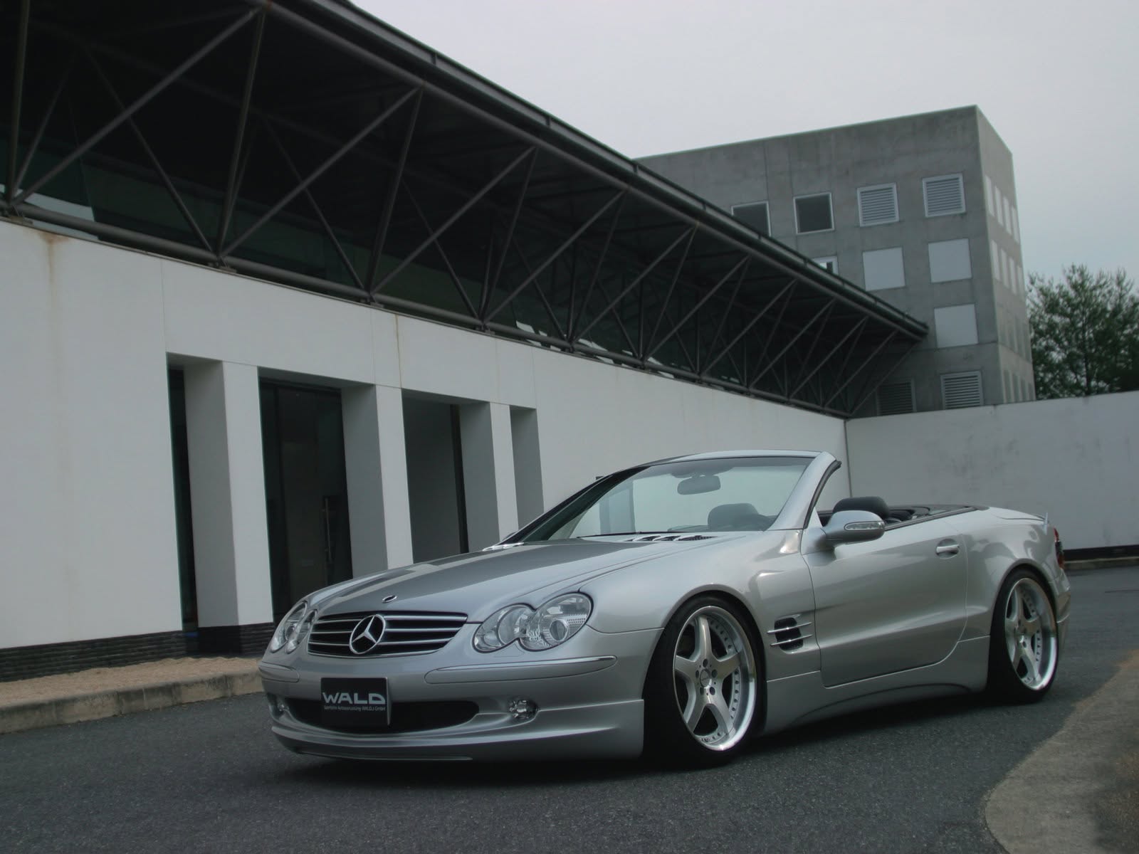 WALD Executive Line Mercedes-Benz SL R230 front three-quarter view with roof down beneath a steel truss canopy
