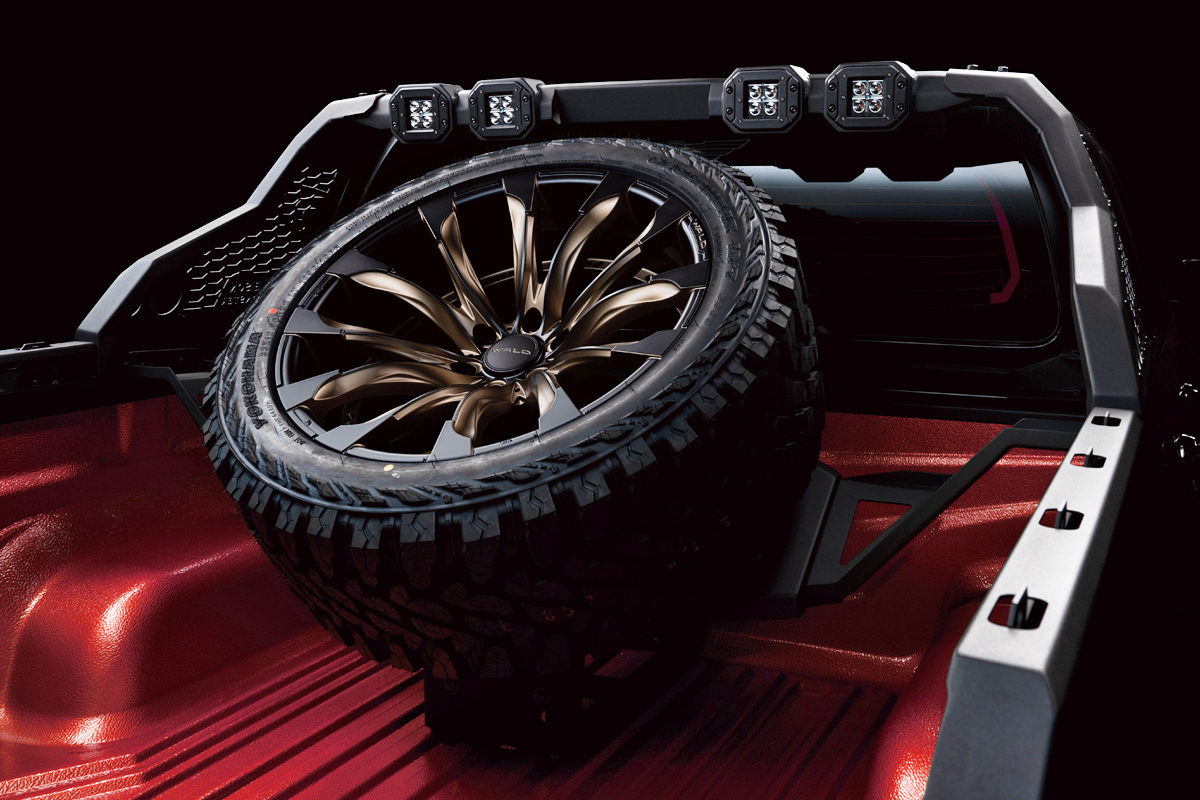 Bronze WALD wheel and off-road tyre carried on the Black Bison spare tyre hanger in the Hilux GUN125 load bed