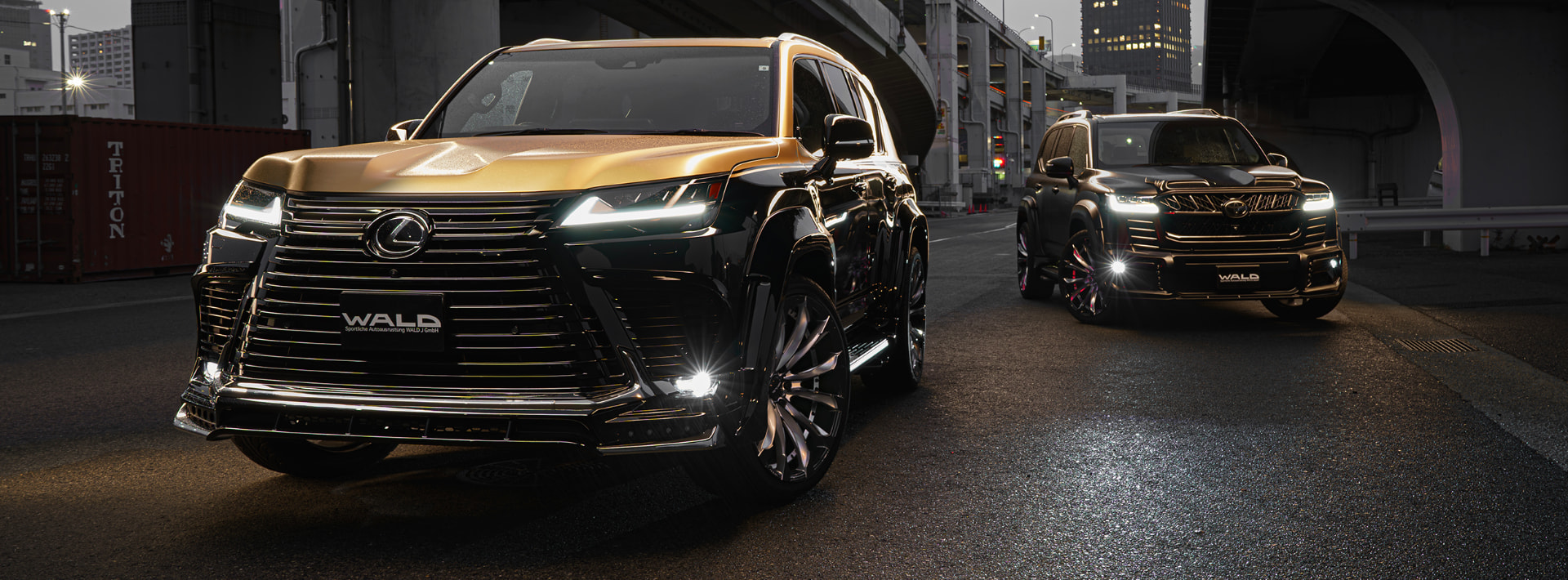 Black Lexus LX and Toyota Land Cruiser with WALD Black Bison styling on an urban highway at dusk