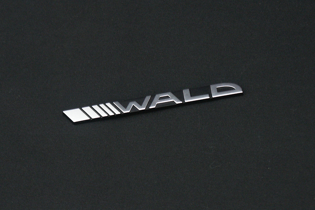WALD Front Emblem in chrome, slash-bar WALD lettering photographed on a black fabric surface