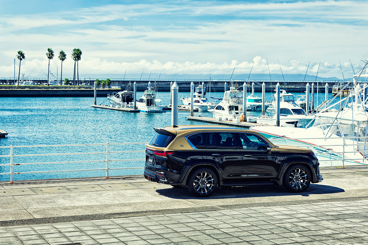 WALD Lexus LX600 Black Bison rear three-quarter at a harbour — rear roof spoiler and wide arch package in profile
