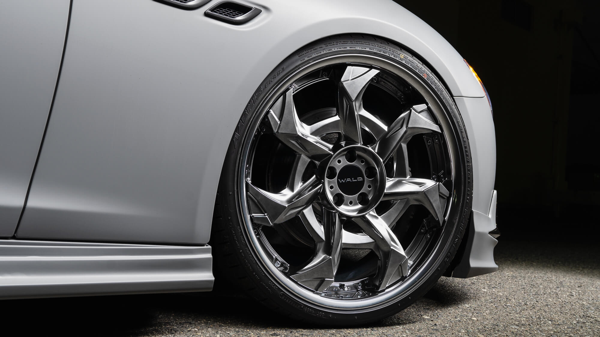 Close-up of a WALD Vorsalino V12C wheel in hyper silver fitted to a matte grey Maserati