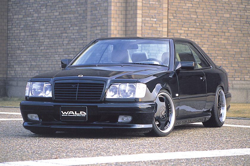 Black Mercedes-Benz E-Class Coupe C124 with WALD V4 body kit — front three-quarter view with WALD front spoiler and forged wheels
