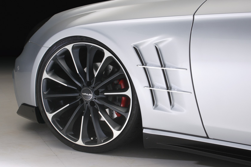 WALD Mercedes-Benz CLS C219 front wheel and sports fender duct detail — multi-spoke WALD wheel with red brake calipers and aluminium fin fender vents