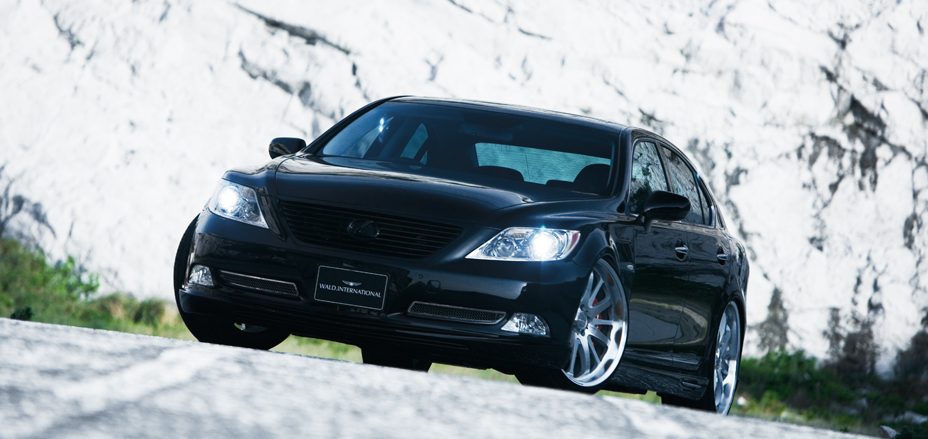 Black WALD Executive Line V1 Lexus LS460L front three-quarter view against a white rock face