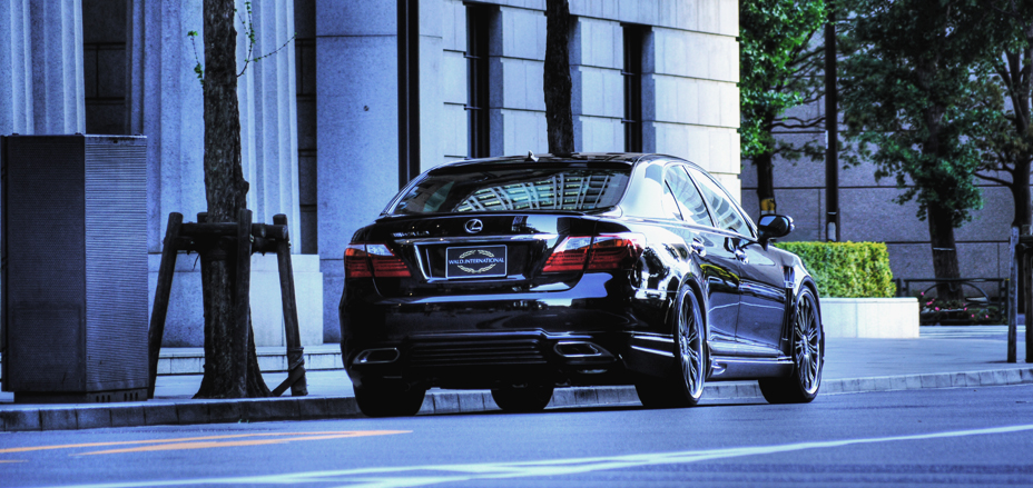 Black WALD Executive Line Lexus LS460L rear view parked on a tree-lined city street