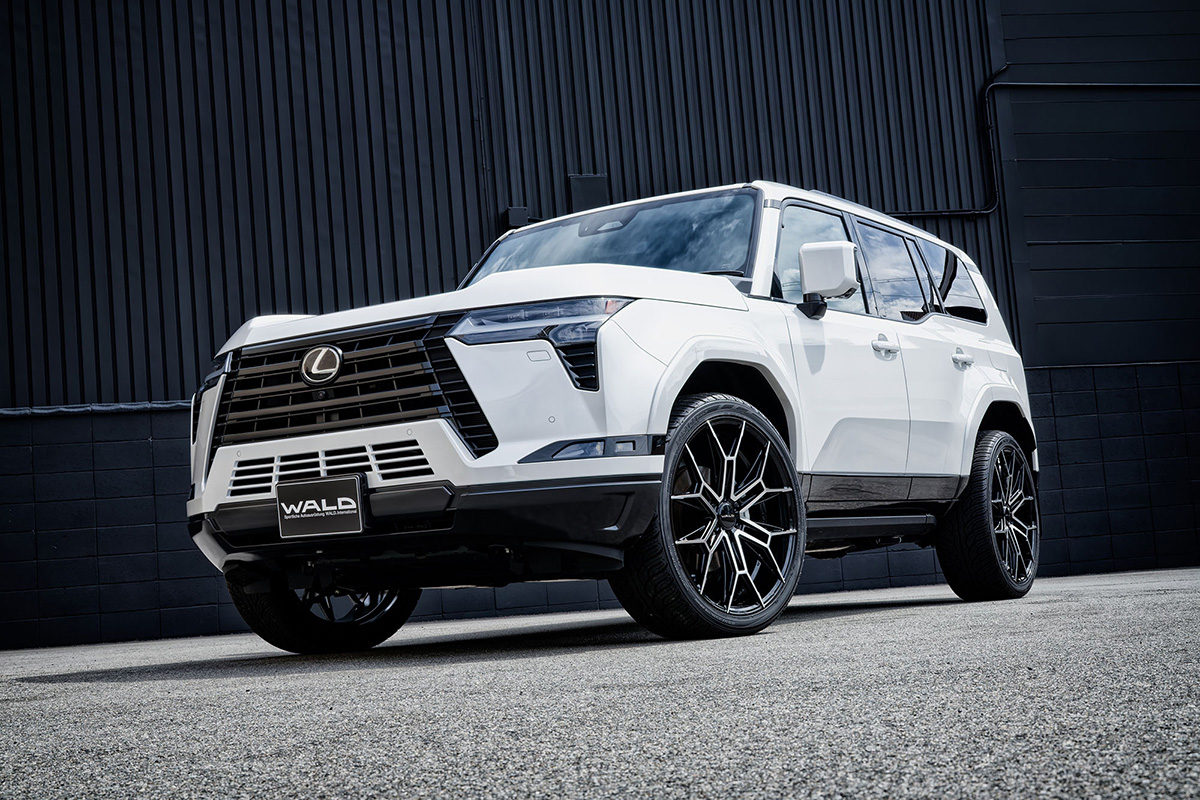 White Lexus GX550 fitted with WALD ELDORANTE E11C 24-inch wheels — front three-quarter view against a dark wall