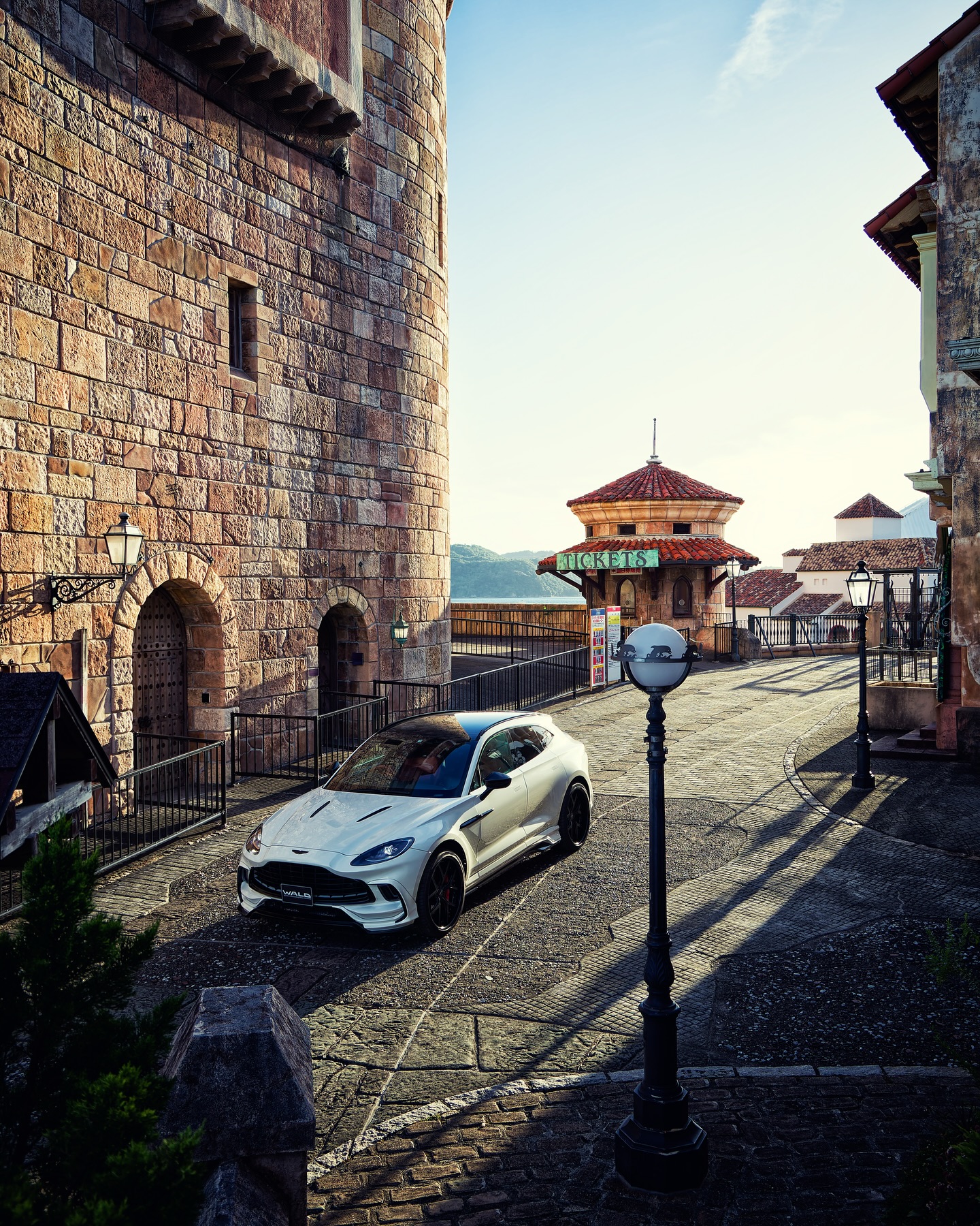 WALD Aston Martin DBX — white DBX parked on a cobbled European-style street, front three-quarter view with WALD front lip spoiler