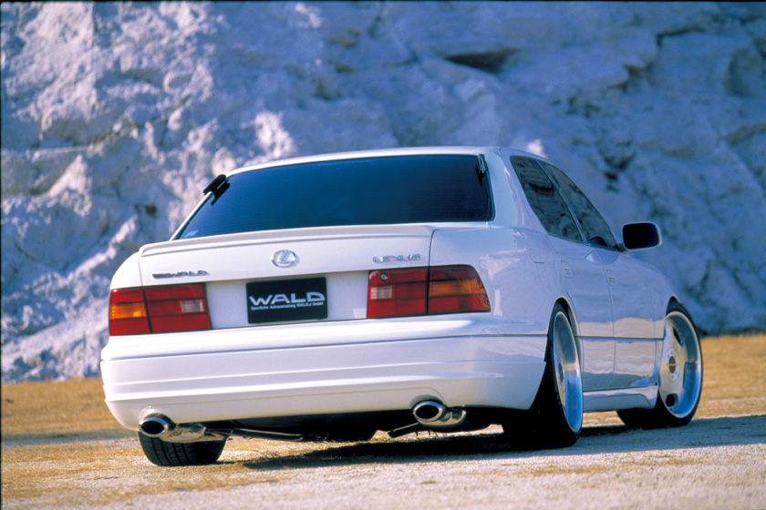 WALD Executive Line Toyota Celsior UCF20/21 M/C before — white Celsior rear three-quarter view in a rocky quarry with WALD rear skirt and dual exhaust outlets
